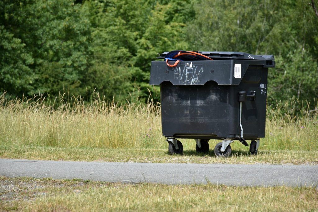 A trash bin sits beside a path.